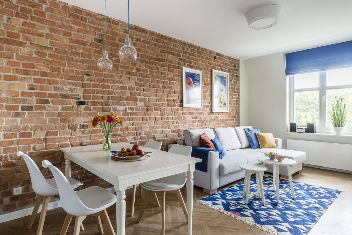Una sala de estar moderna con pared de ladrillo, muebles blancos y alfombra azul estampada.