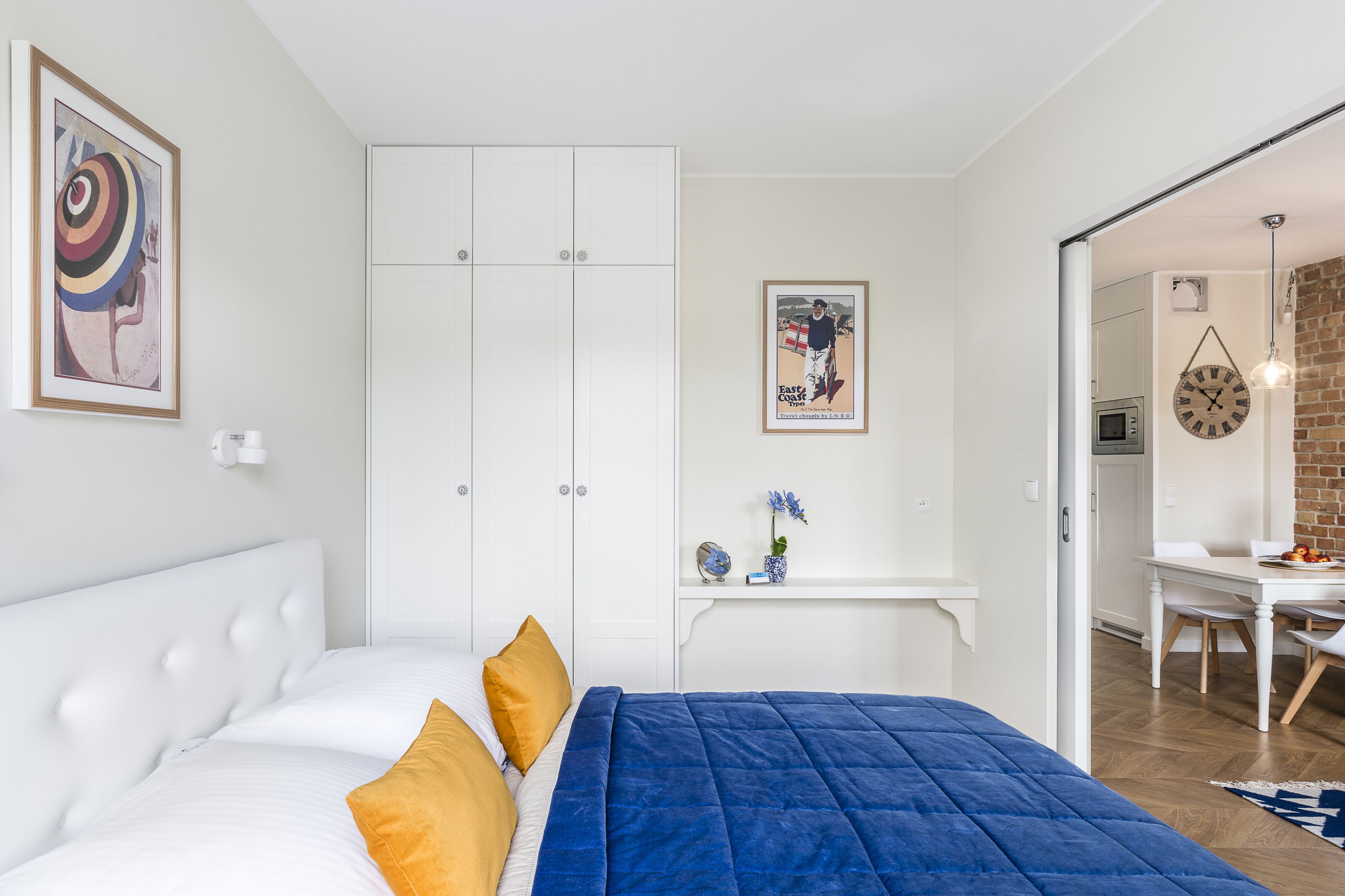 Un dormitorio con cama, armario blanco, escritorio y zona de comedor.