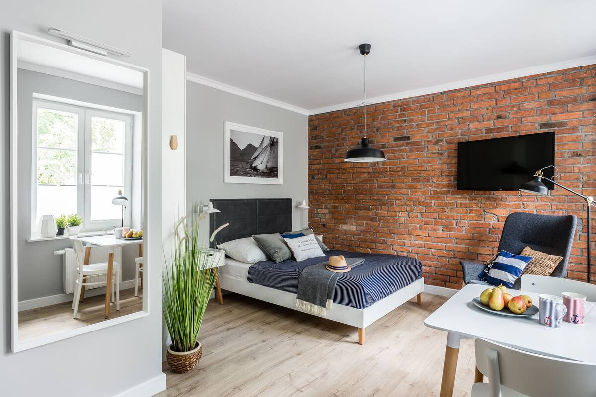 Un dormitorio moderno con pared de ladrillo, una cama con cabecera, una mesa de comedor con frutas y un televisor montado en la pared.