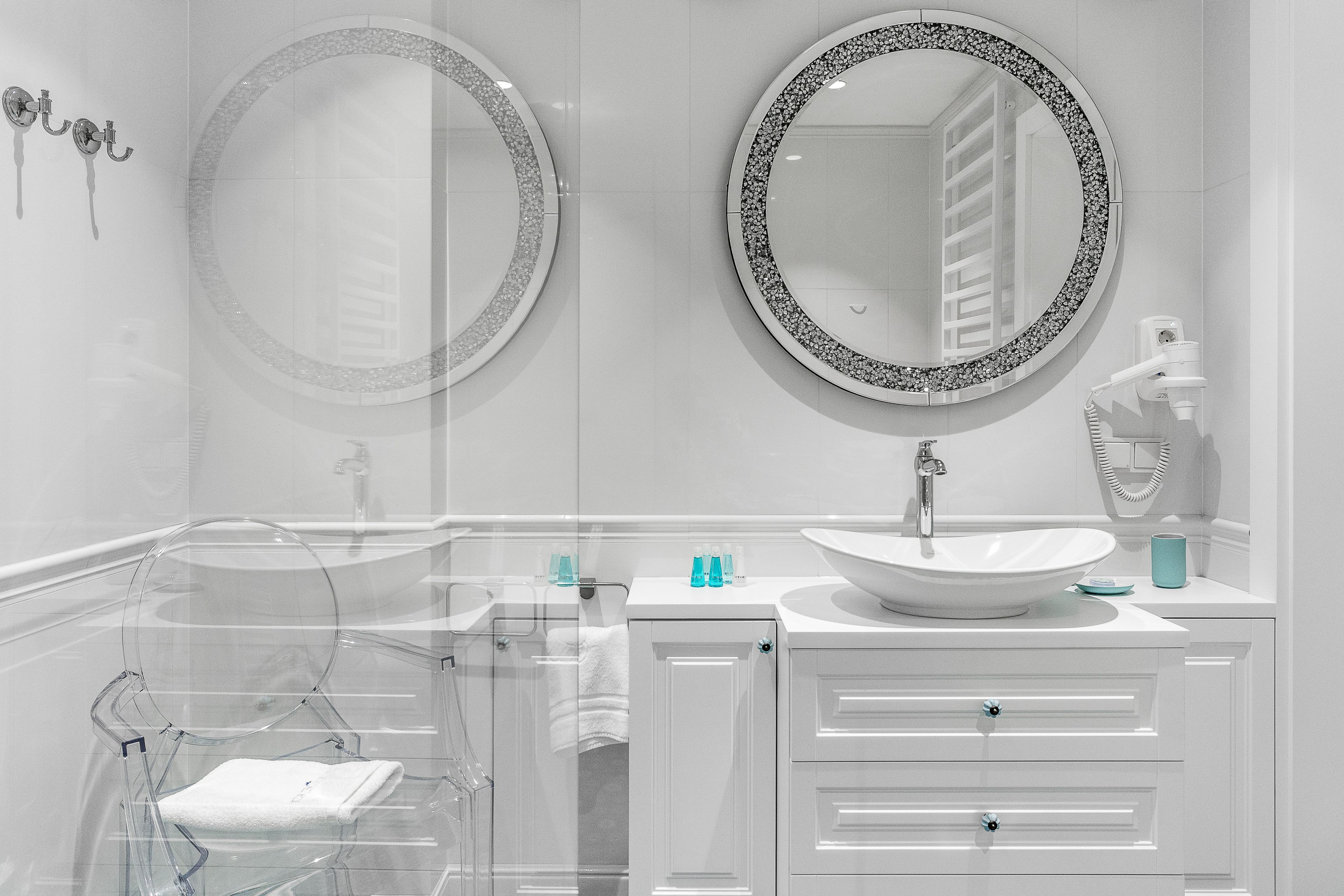 Ein modernes Badezimmer mit zwei runden Spiegeln, einem weißen Waschbecken und einer Duschkabine aus Glas.