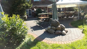 A patio area with outdoor seating, a stone centerpiece, and a building in the background. - Landgasthof Allerparadies (Langlingen)