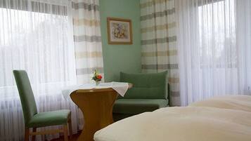Une pièce comprenant un lit, une chaise, une petite table avec un vase de fleurs et un tableau accroché au mur.