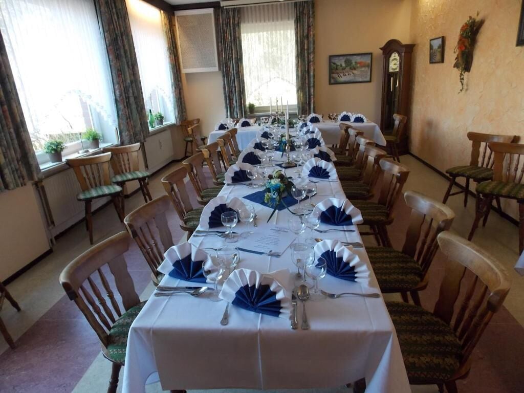Una larga mesa de comedor preparada para una comida formal, con sillas, un menú y un centro de mesa con velas.