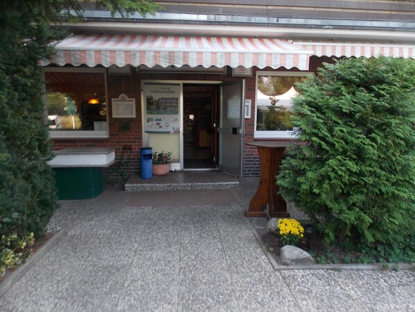 A storefront with a striped awning, a brick facade, and a small outdoor seating area with a table and chairs. - Landgasthof Allerparadies (Langlingen)