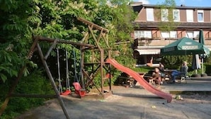 A playground with swings and a slide, surrounded by trees and a building in the background. - Landgasthof Allerparadies (Langlingen)
