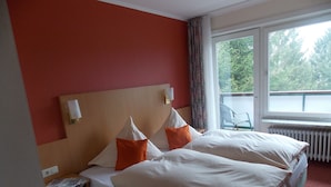 A hotel room with two beds, a window with a view of greenery, a radiator, and a chair outside the window. - Landgasthof Allerparadies (Langlingen)