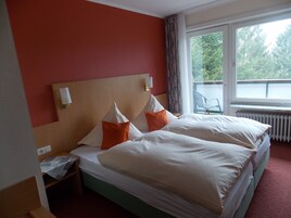 Habitación de hotel con dos camas, una ventana que da a zonas verdes, un radiador y una silla junto a la ventana.