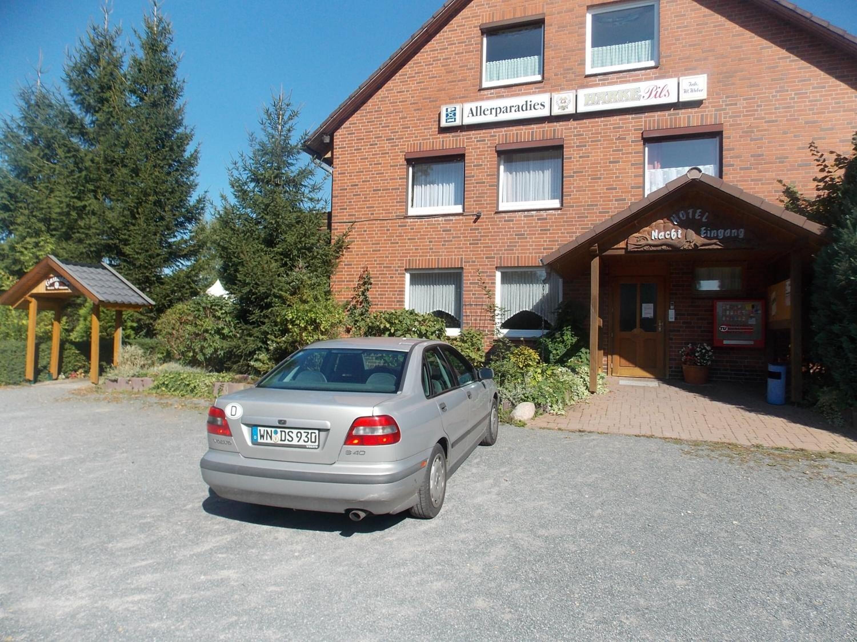 Ein Hotel mit Ziegelaußenwand, einem Schild mit der Aufschrift 'Allerparadies' und einem geparkten Auto davor.