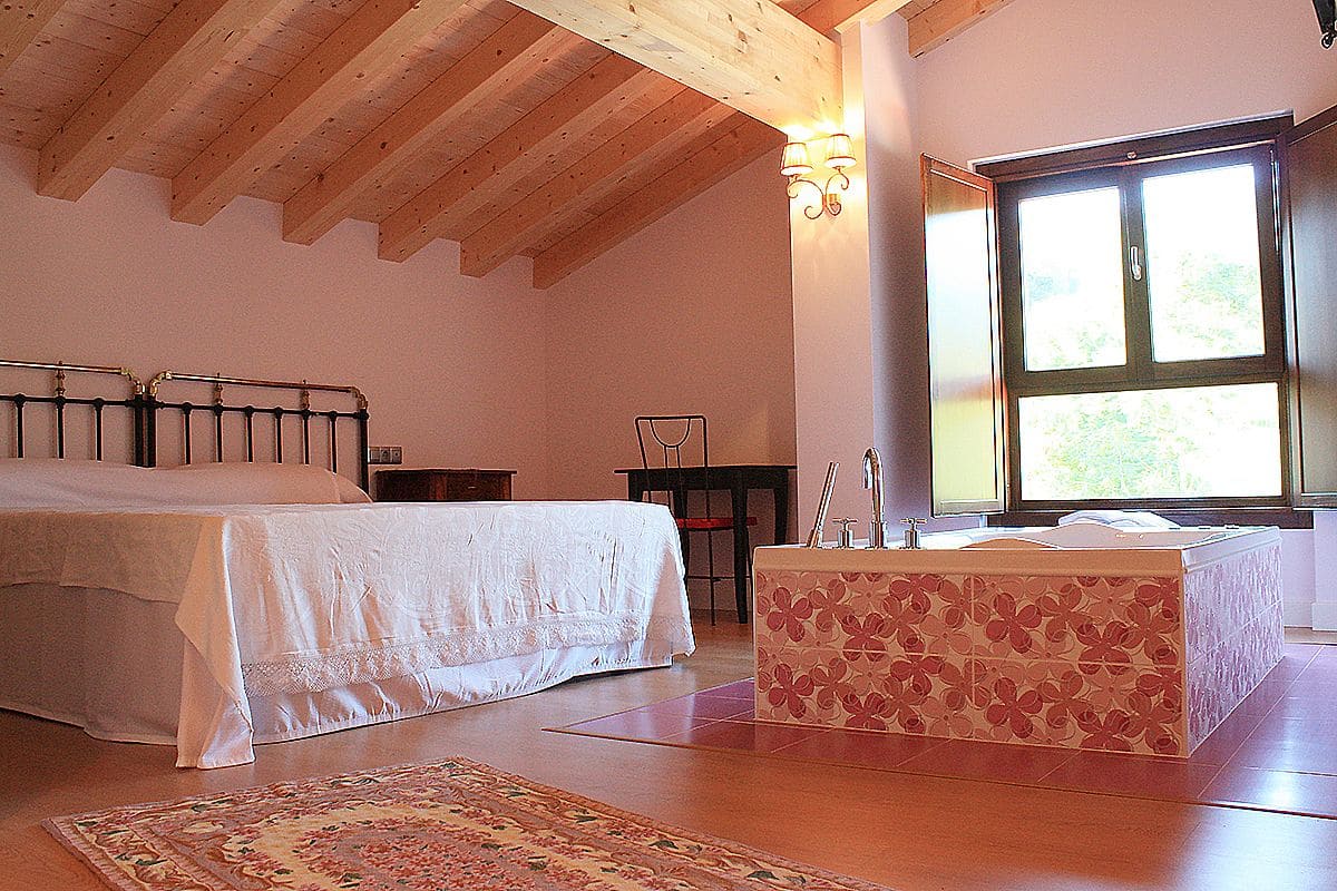 A bedroom with a bed, a wooden ceiling, a window, and a small table.