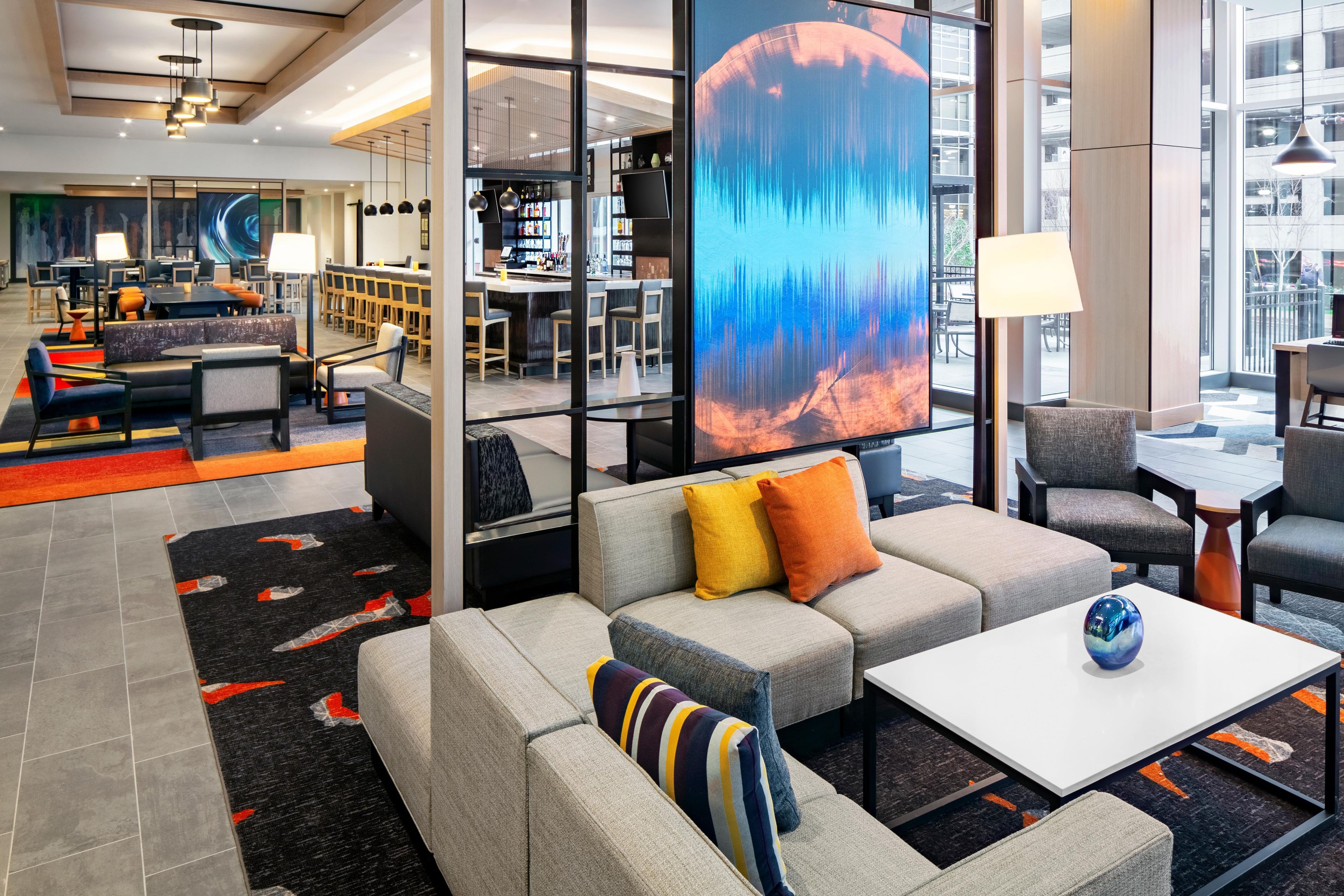A modern hotel lobby with a seating area, a bar, and a large digital screen displaying an abstract image.