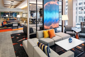En moderne hotellobby med et siddeområde, en bar og et stort digitalt skærm, der viser et abstrakt billede.