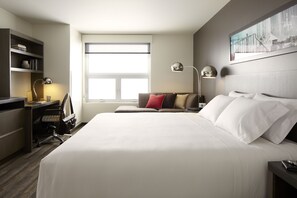 Una habitación de hotel con una cama grande, un escritorio con silla, una estantería y un ventanal.