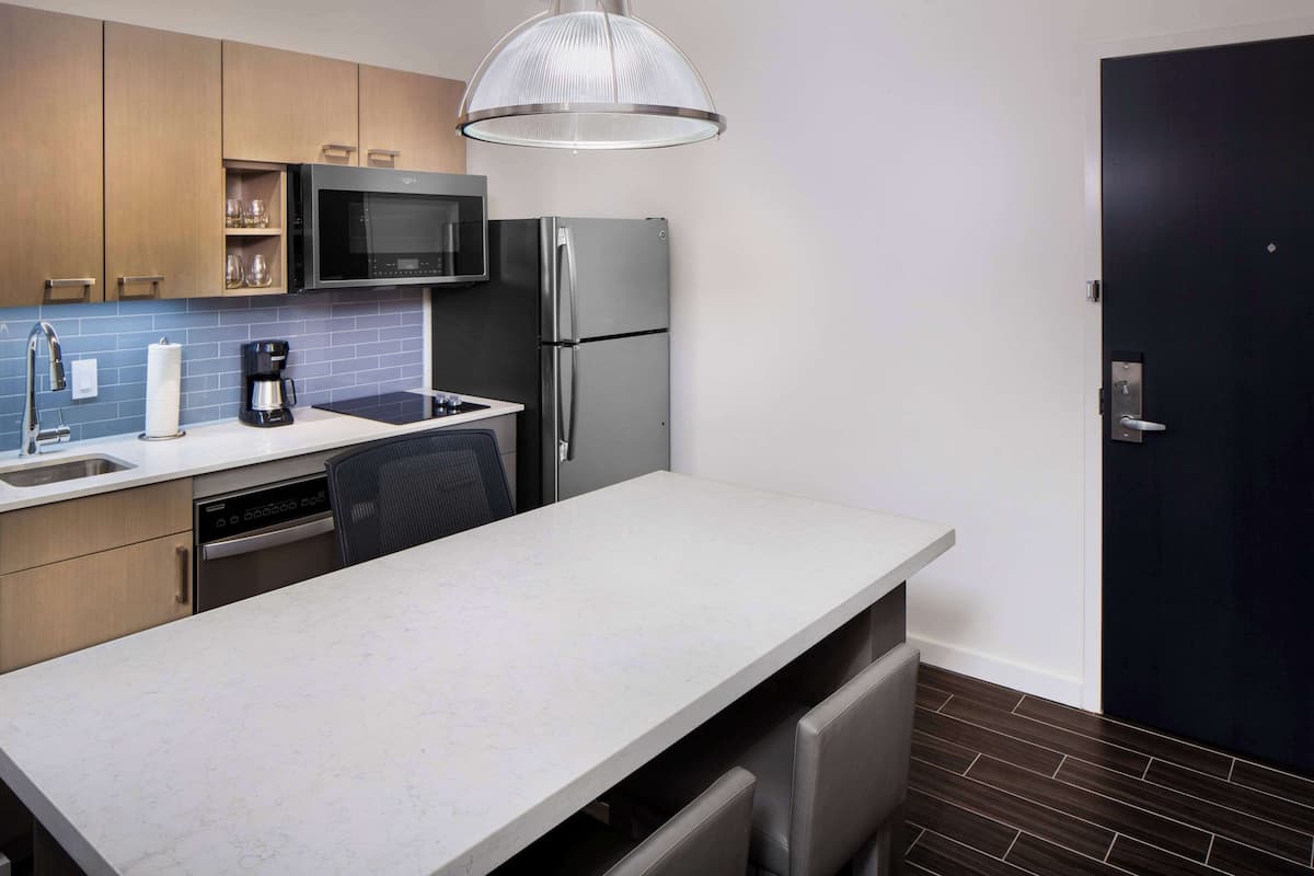 A modern kitchen with a built-in microwave, stainless steel refrigerator, and a large island with a sink.