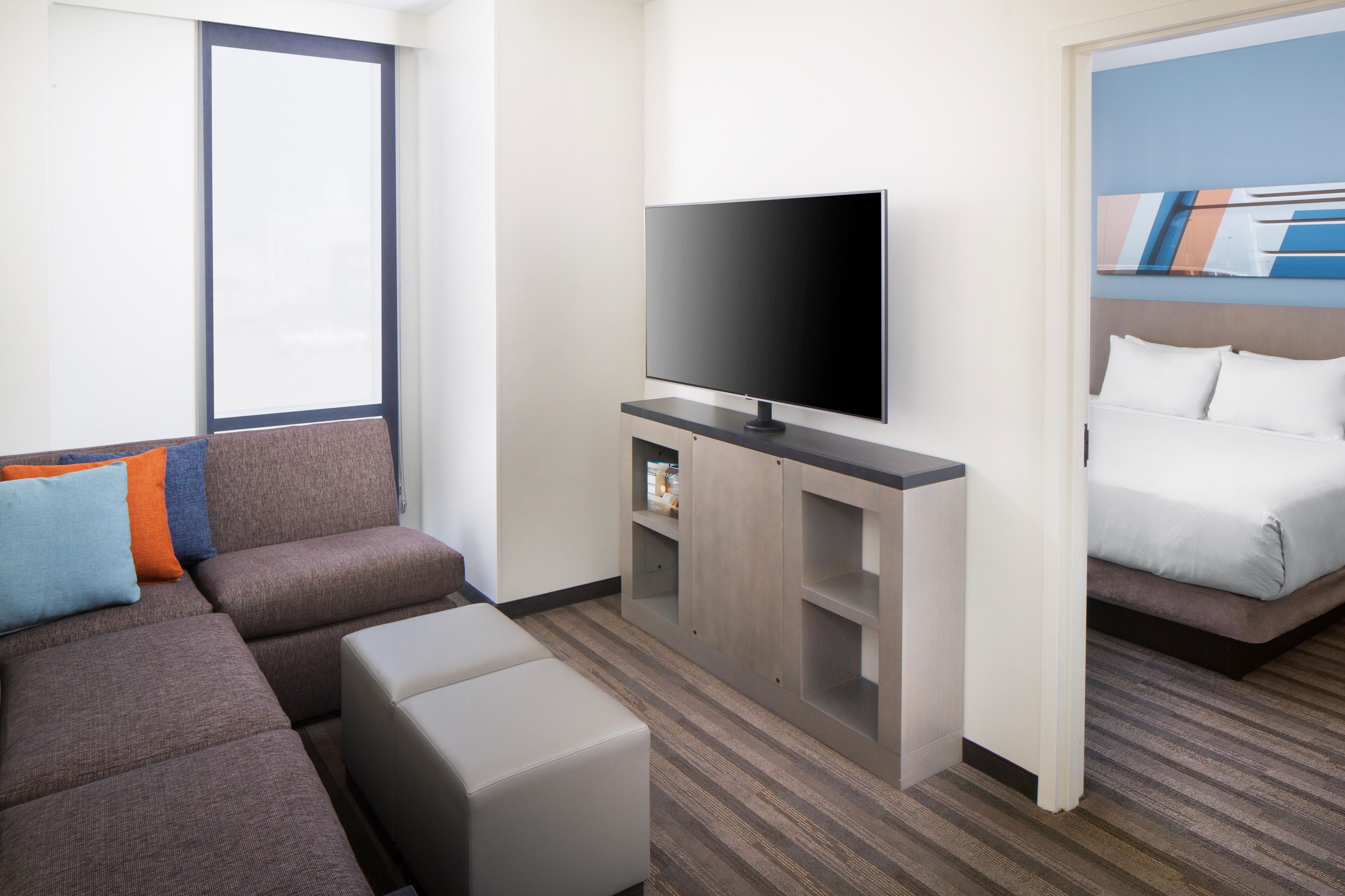 A hotel room with a sofa, ottoman, flat-screen TV, and a bed.