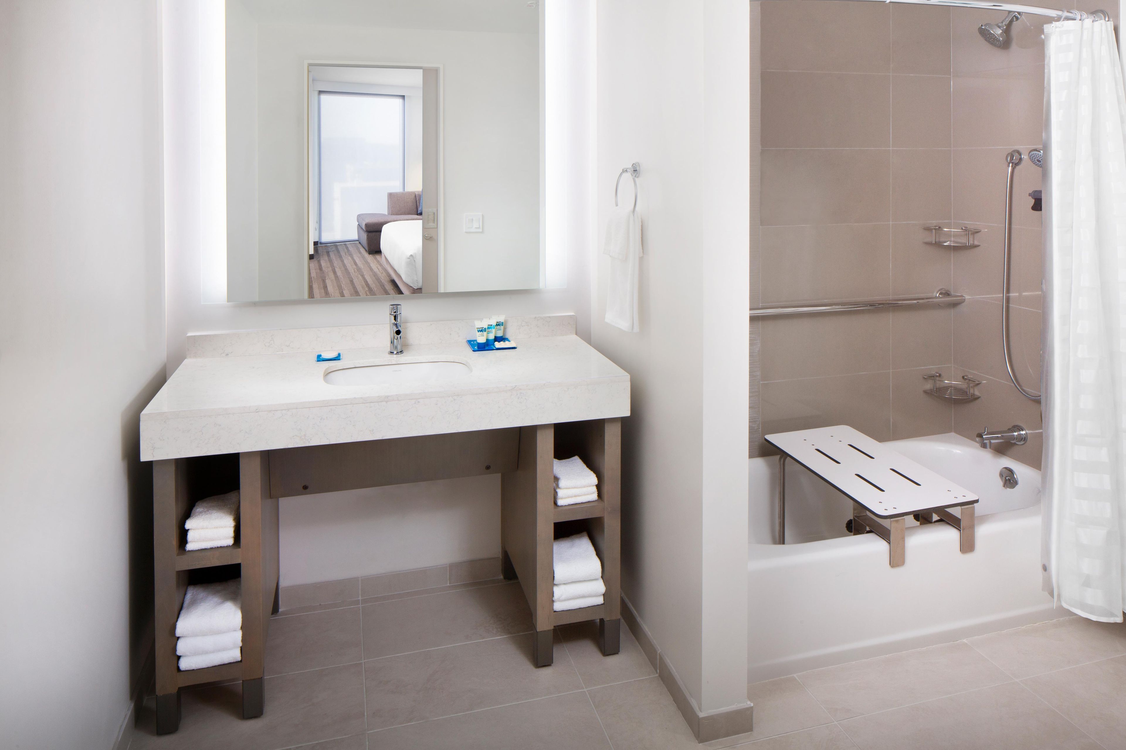 Un baño con lavamanos, espejo, toallero y ducha.