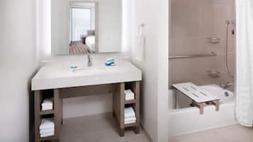 Un baño con lavamanos, espejo, toallero y ducha.