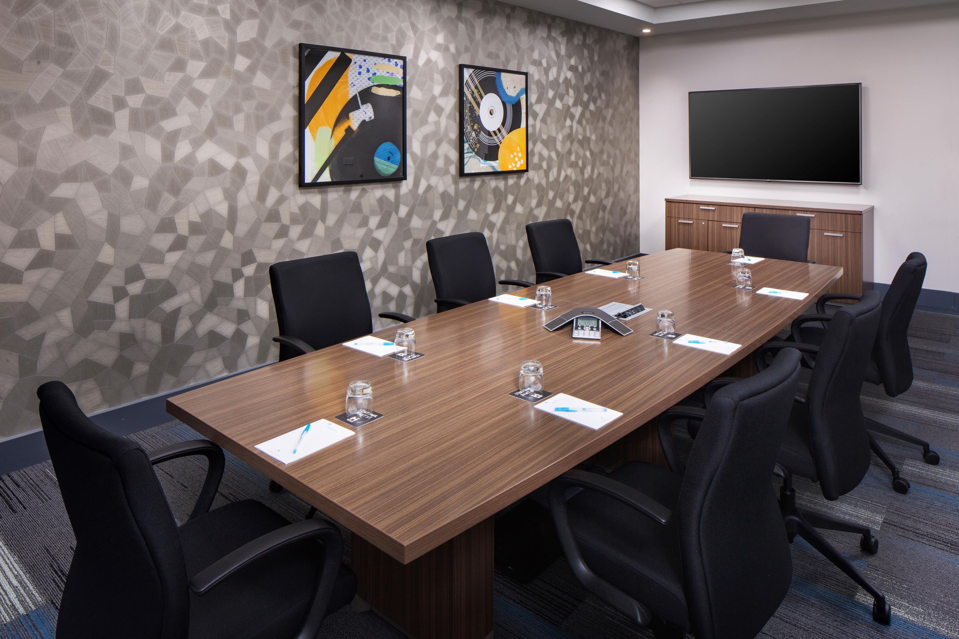 A conference room with a long table, black chairs, a flat-screen TV, and abstract art on the wall.