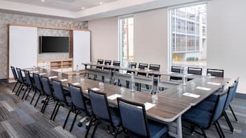 A conference room with a long table, chairs, a flat-screen TV, and a whiteboard.