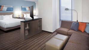 A hotel room with two beds, a sofa, a desk, and a large window.