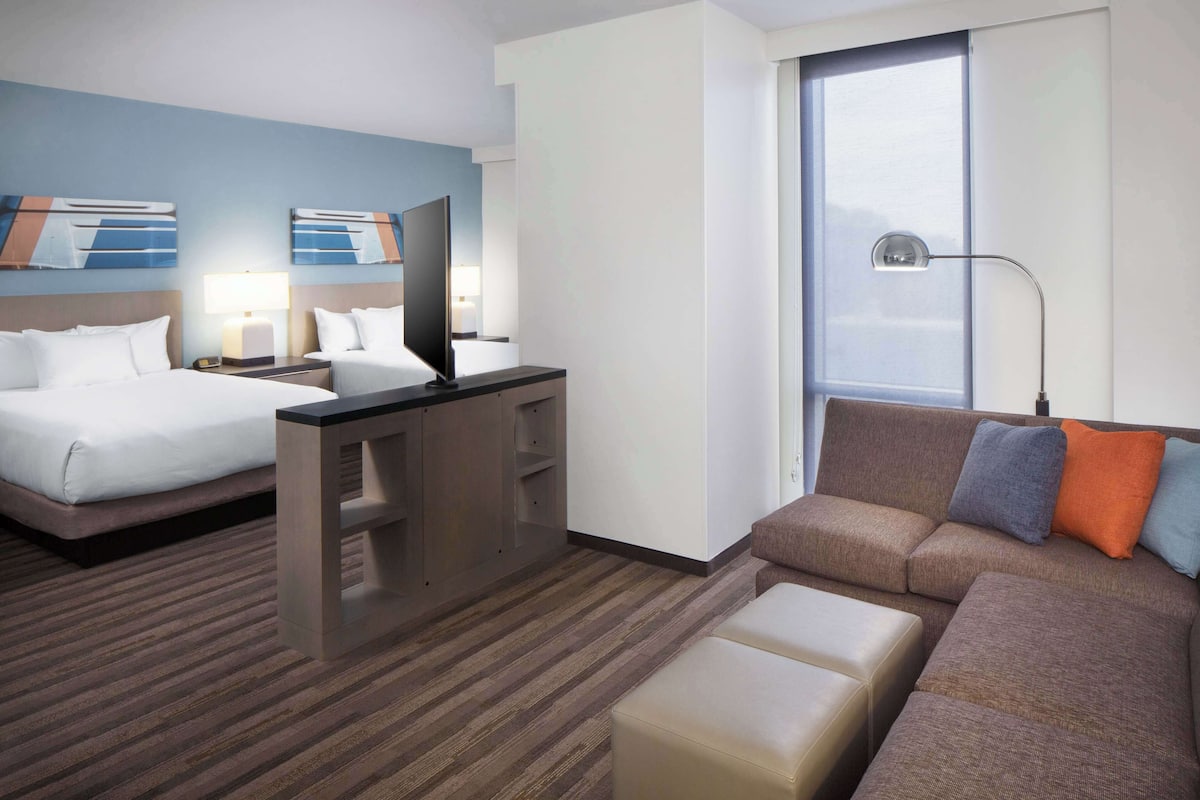 A hotel room with two beds, a sofa, a desk, and a large window.
