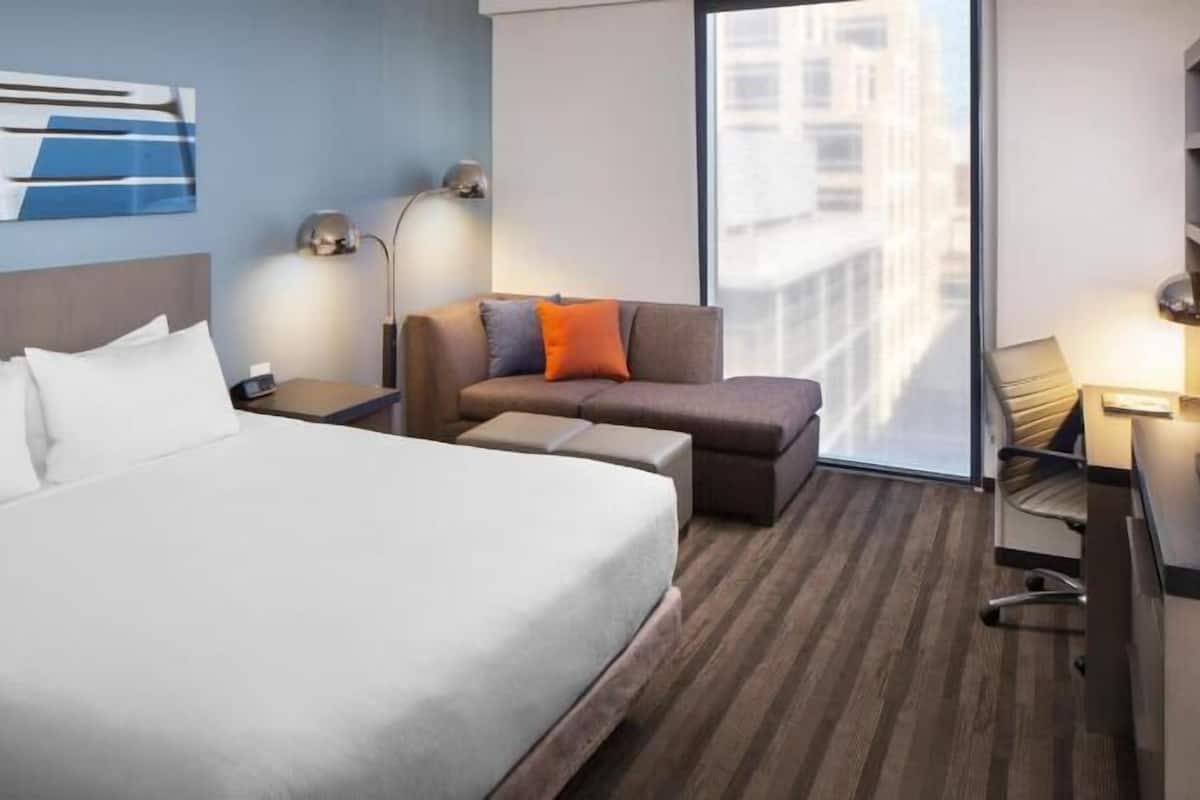 A hotel room with a large bed, a sofa, a desk, and a chair.