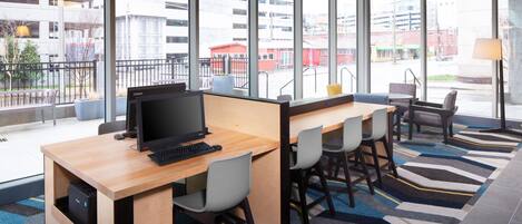 Un espace de bureau moderne doté d’une grande fenêtre, d’un bureau avec un ordinateur et de plusieurs chaises.