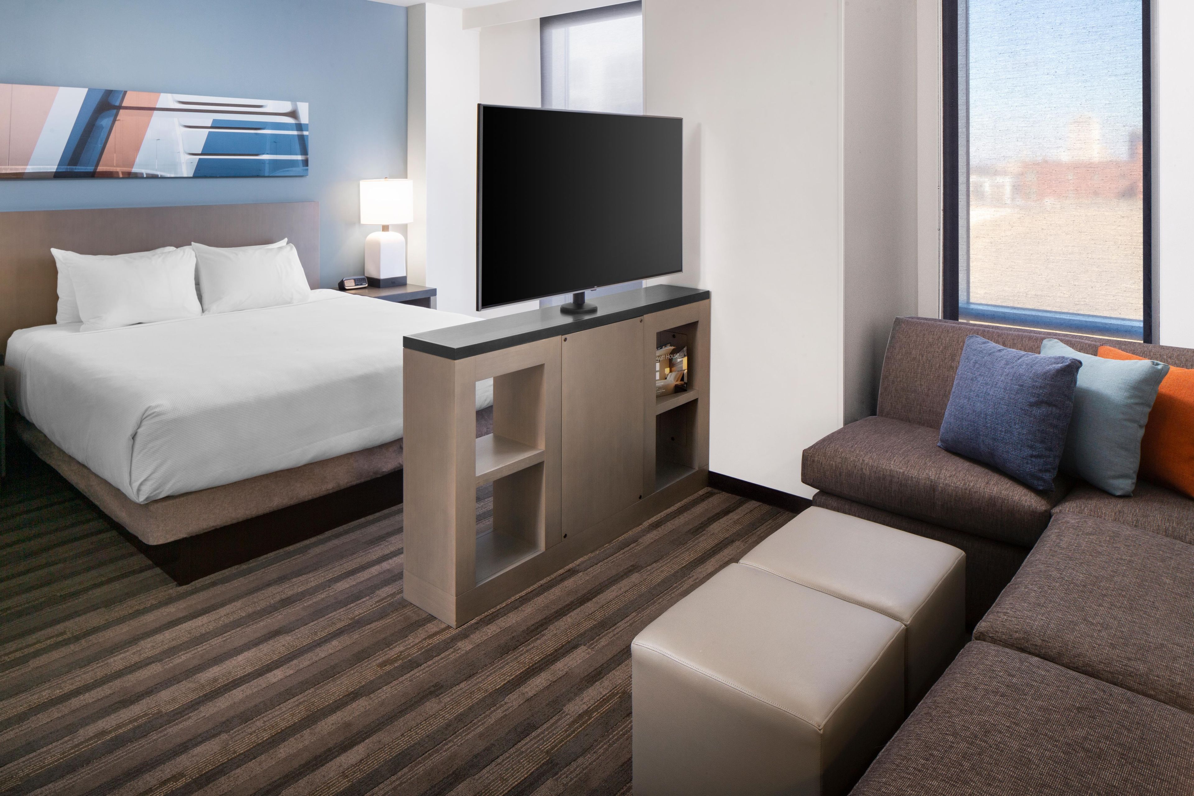 Una habitación de hotel con cama, televisión, sofá y ventana.