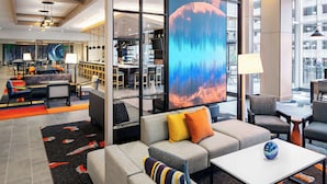 A modern hotel lobby with a seating area, a bar, and a large digital screen displaying a landscape.