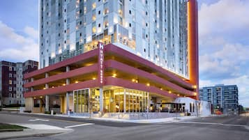 Un hotel de varios pisos con un diseño moderno, que destaca por su fachada roja y blanca, grandes ventanales y una entrada accesible con rampa.