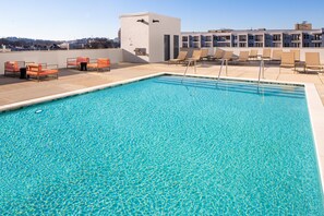 A rectangular swimming pool with clear blue water, surrounded by lounge chairs and a building with multiple balconies in the background. - Hyatt House Nashville at Vanderbilt (Nashville)