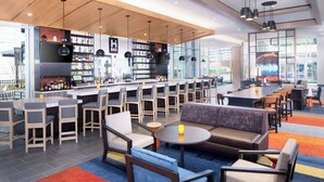 A modern bar area with seating and a bar counter, featuring a mix of bar stools and sofas, and a large window providing a view of the outside.