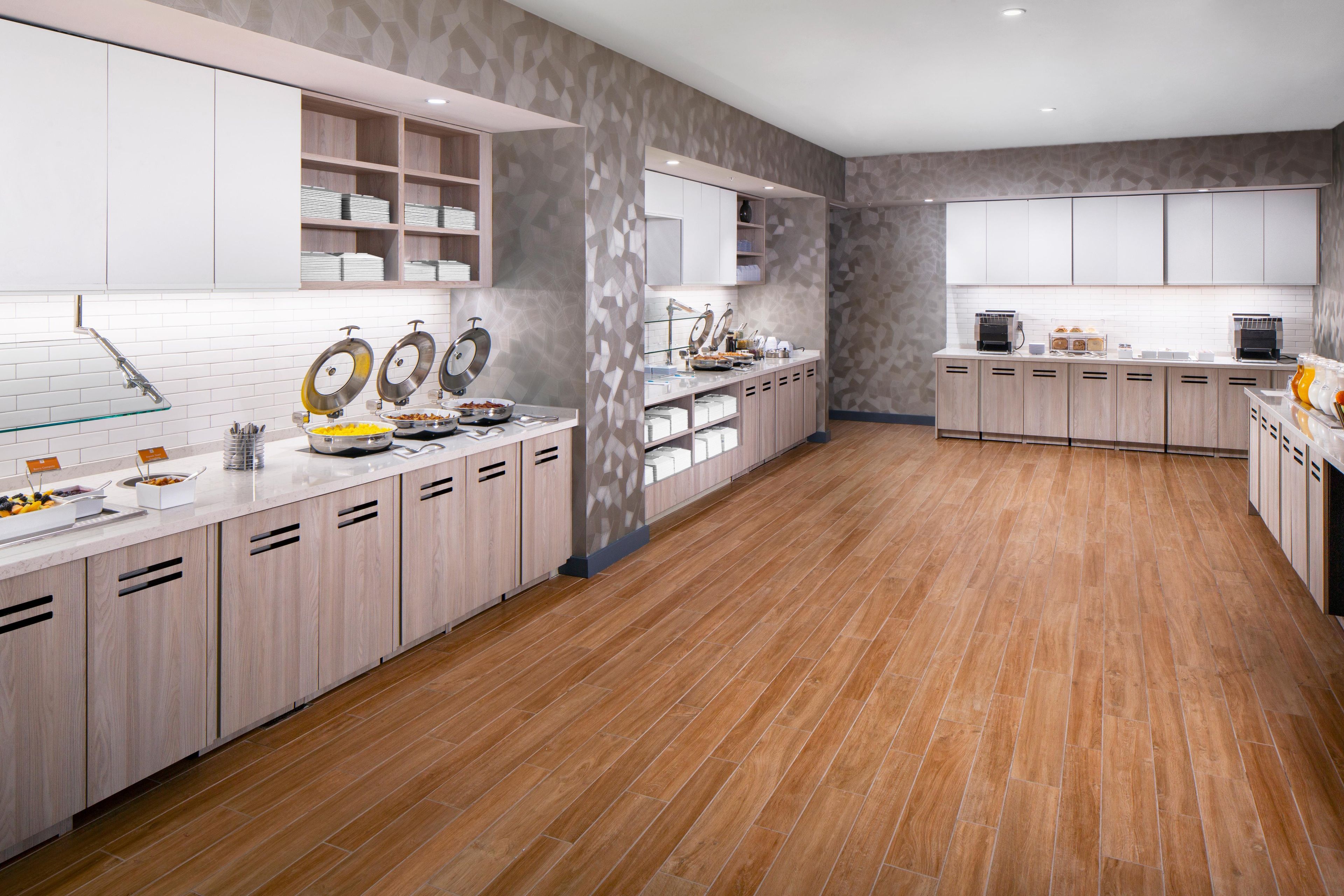 A modern kitchen with white cabinets, a wooden floor, and a breakfast bar with various food items.