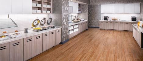 A modern kitchen with white cabinets, a wooden floor, and a breakfast bar with various food items.