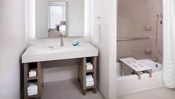 Une salle de bain équipée d’un lavabo, d’un miroir, d’un porte-serviettes, d’une douche et d’une petite étagère.