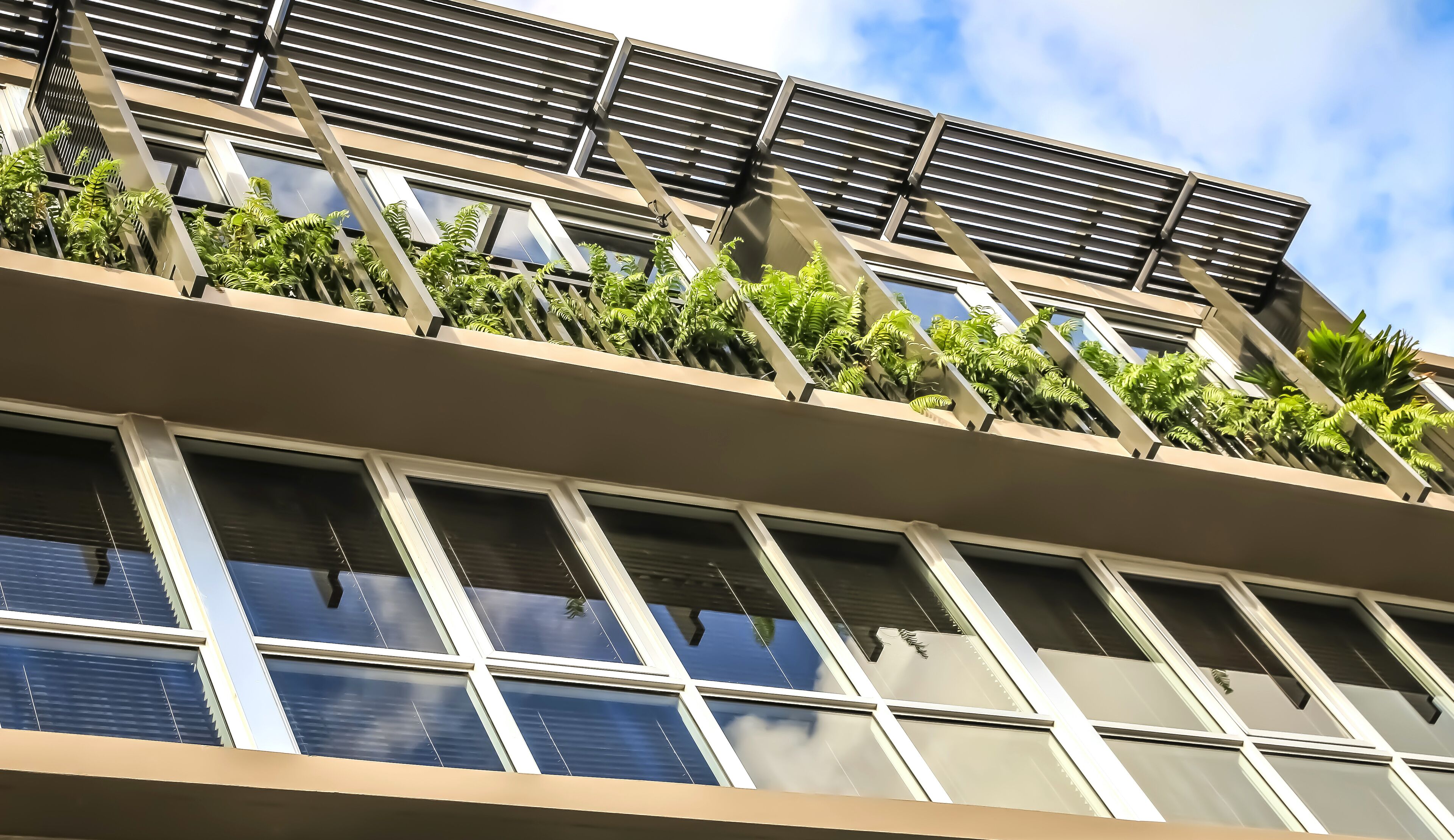 Un edificio moderno con diversi piani, ampie finestre e piante verdi sui balconi.