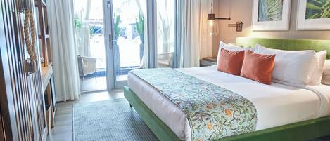 A hotel room with a large bed, a green headboard, and a view of the outdoors through a sliding glass door.