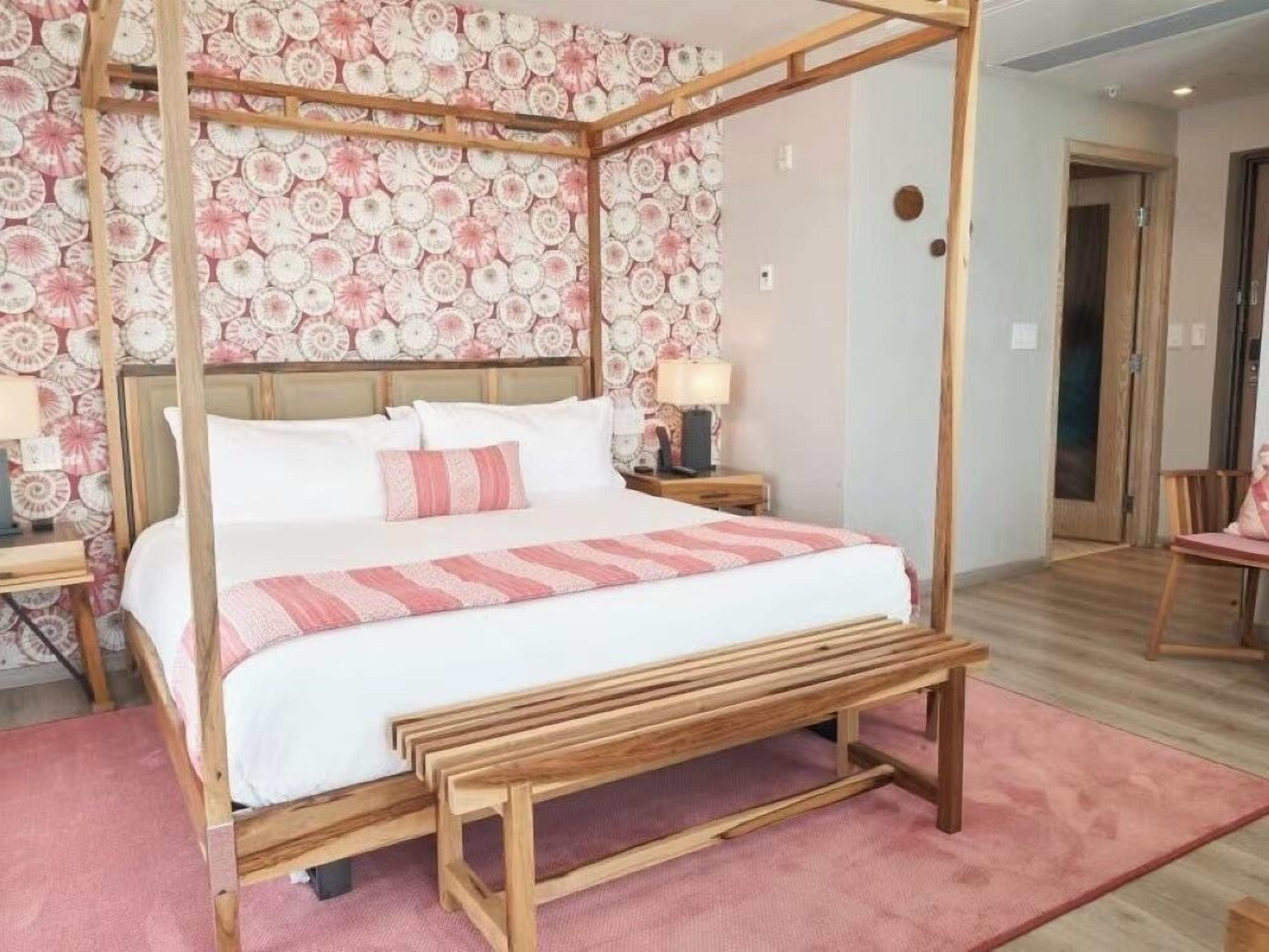 A four-poster bed with a wooden frame, a pink and white striped bedspread, and a matching pillow.