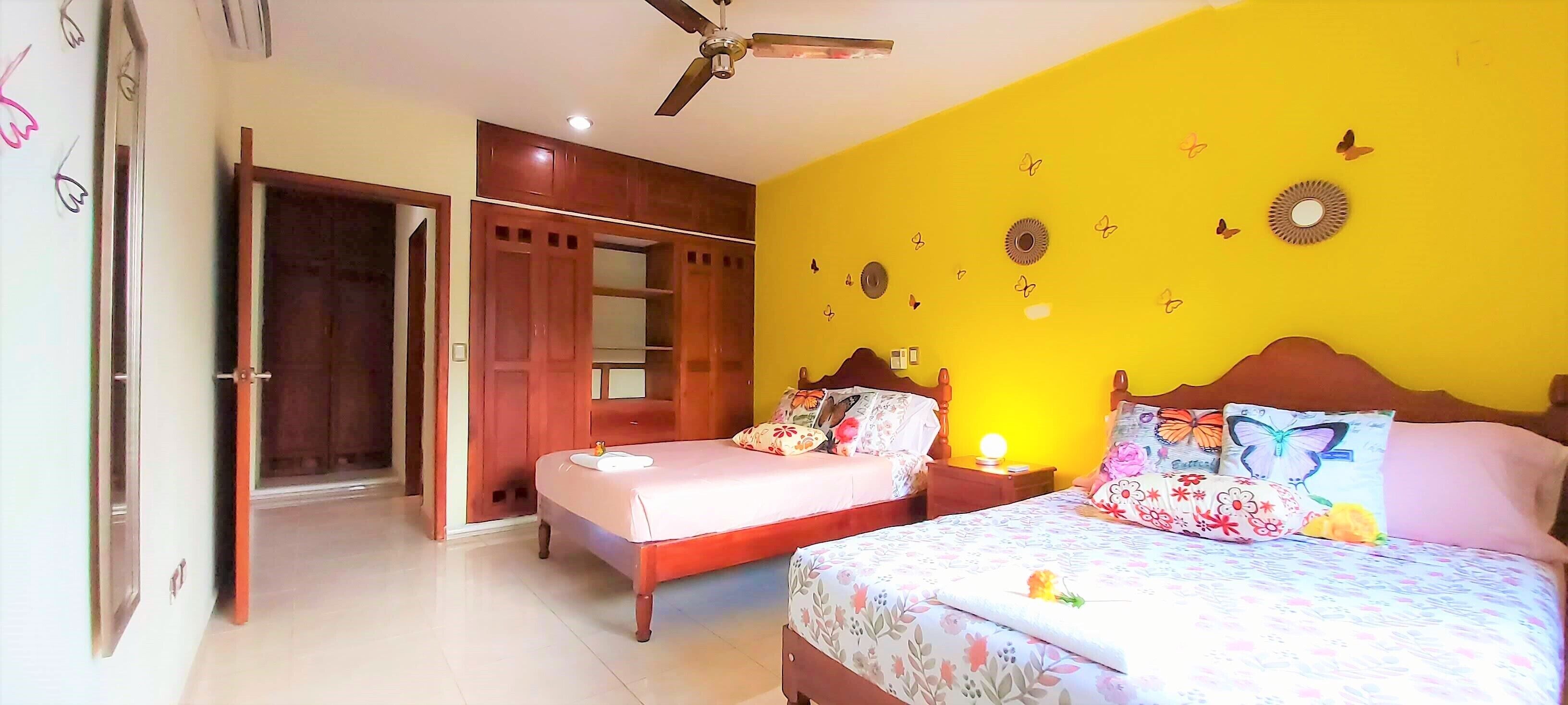 Un dormitorio con dos camas, armarios de madera, ventilador de techo y decoración de mariposas en la pared.