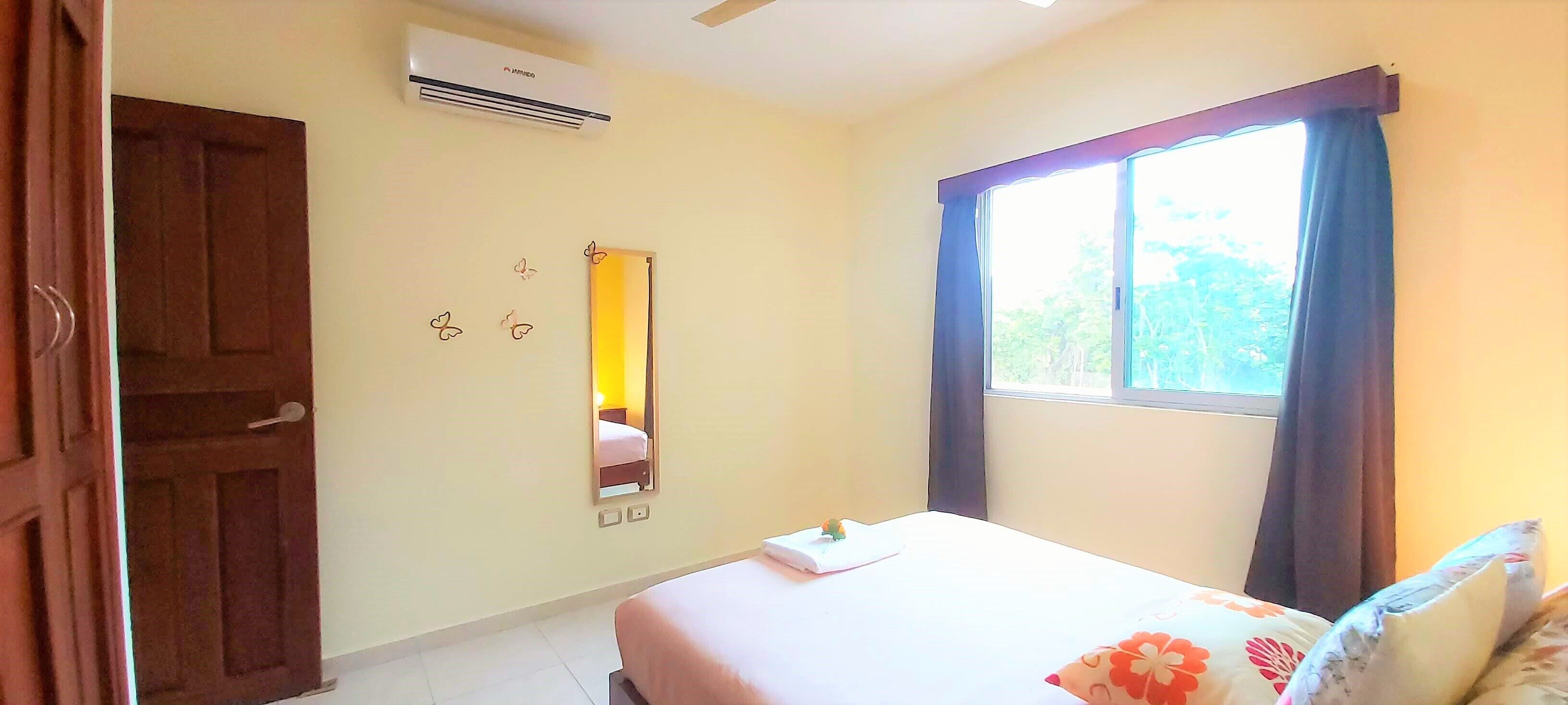 Habitación de hotel con cama, ventana con cortinas, aire acondicionado de pared y puerta.