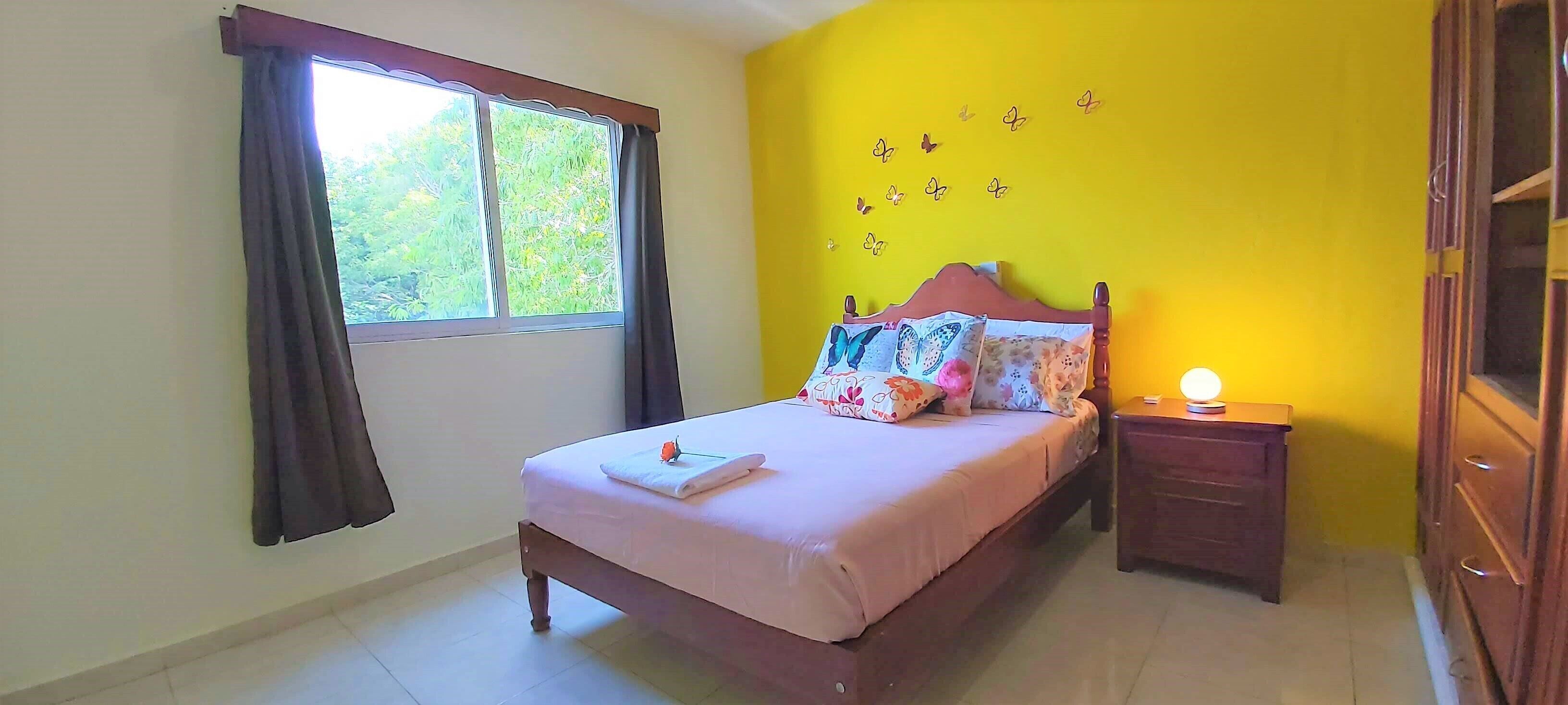 A bedroom with a bed, a nightstand, a window with curtains, and a wall with butterfly decals.