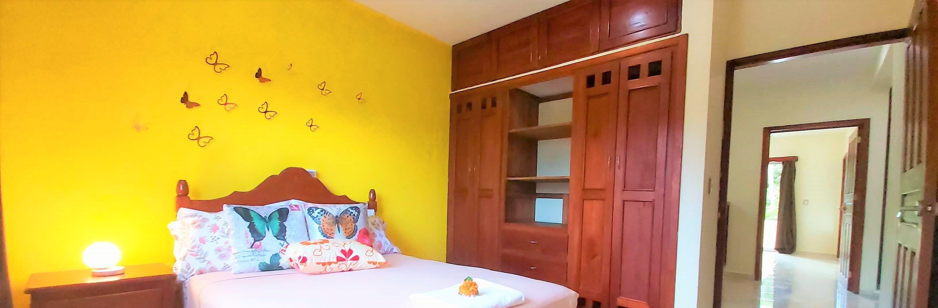 A bedroom with a bed, a nightstand, a wooden wardrobe, and a door leading to another room.