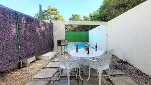 Un'area patio con un tavolo e sedie bianche, una piccola piscina e una recinzione verde.
