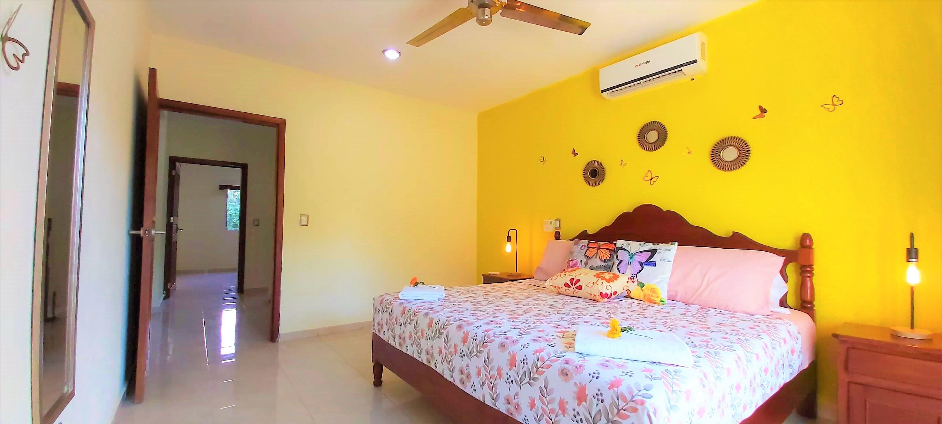 Une chambre à coucher comprenant un lit, une table de chevet, un ventilateur de plafond et un climatiseur fixé au mur.