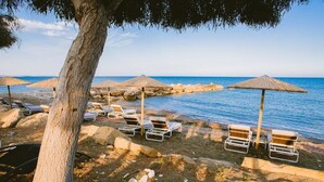 Una playa con sillas de descanso y sombrillas, un litoral rocoso y una vista despejada del mar.