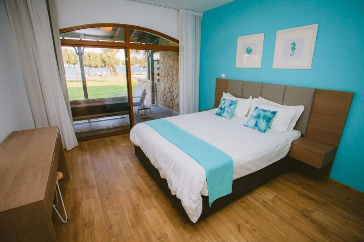 A bedroom with a bed, a desk, and a view of a garden through a glass door.