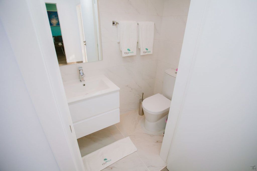 Ein Badezimmer mit Waschbecken, Spiegel und Toilette. Zwei Handtücher hängen an der Wand.