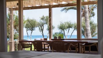 A covered outdoor seating area with a view of the ocean and palm trees.