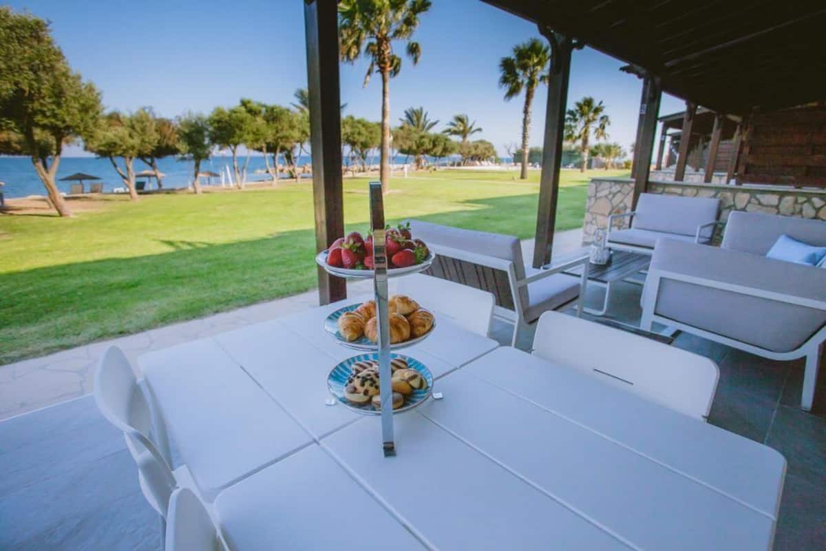 A covered outdoor seating area with a table set for breakfast, overlooking a grassy area and the sea.