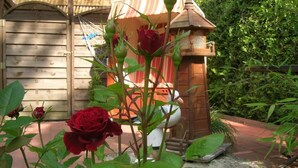 A garden with a wooden structure, possibly a shed, and a rose bush in the foreground. - Hotel Garni Nolting (Esens)