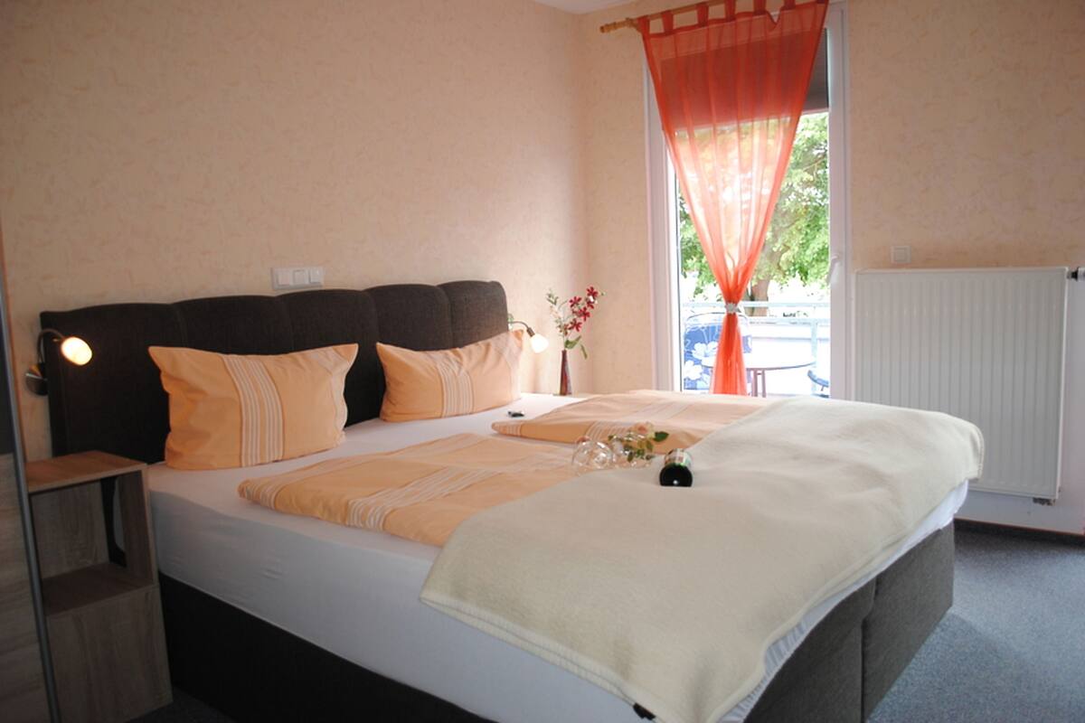 A neatly made bed with a headboard, a bedside table with a lamp, and a window with curtains.